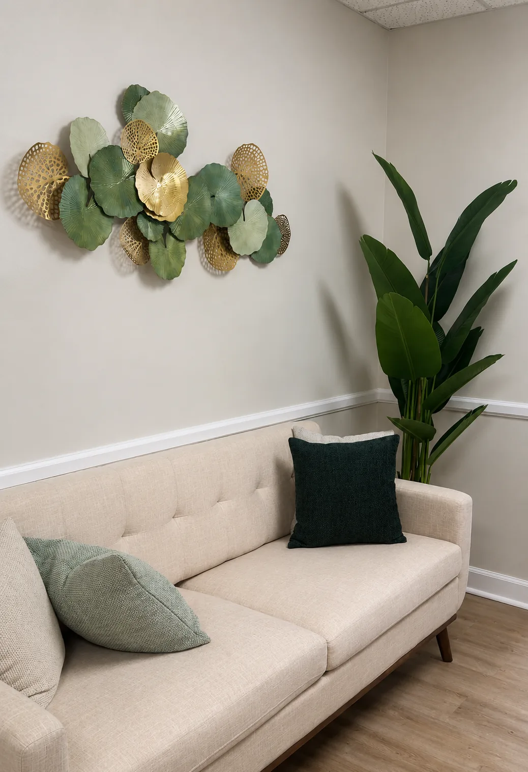Waiting area with a cream sofa, green cushions, a tall potted plant and green-and-gold wall art